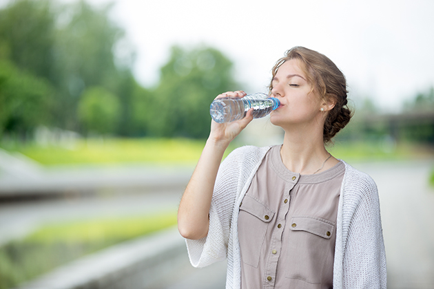 Lifestyle headshot portrait of beautiful woman drinking water with closed eyes. Young female standing on the street and enjoying bottled water in summer. Thirsty attractive caucasian model